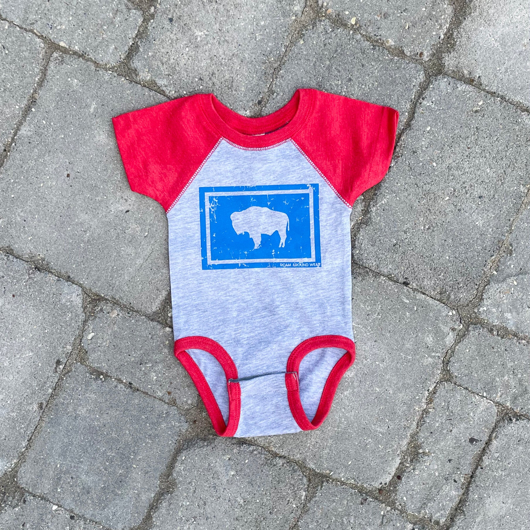 Wyoming flag infant red/gray/blue onesie. Roam Around Wear is a women owned Wyoming T-Shirt company based out of Gillette, Wyoming.